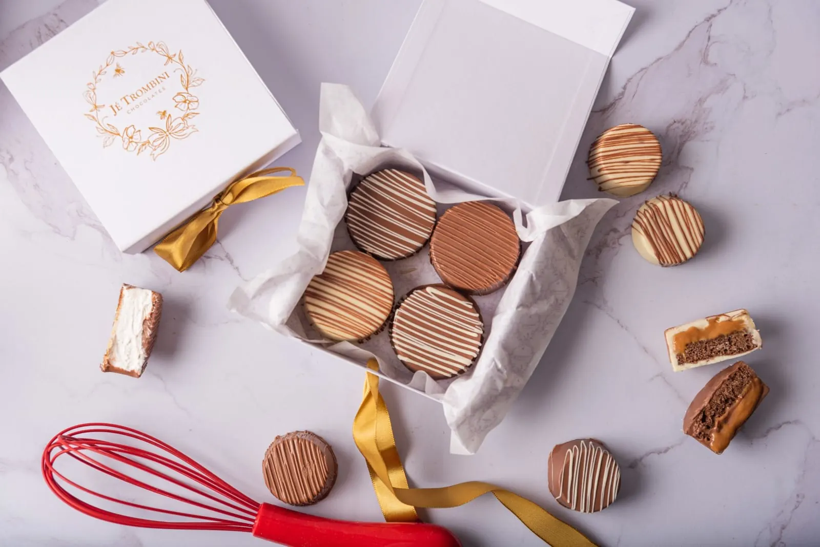 Caixa de presente Jé Trombini com pão de mel coberto de chocolate e laço dourado sobre mármore