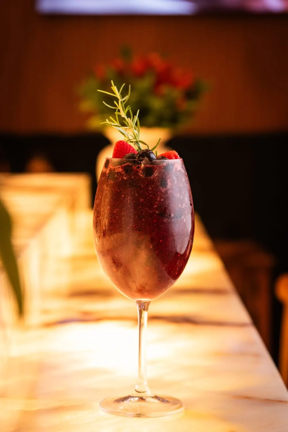 Drink de frutas vermelhas em taça com morango, mirtilo e alecrim sobre balcão iluminado